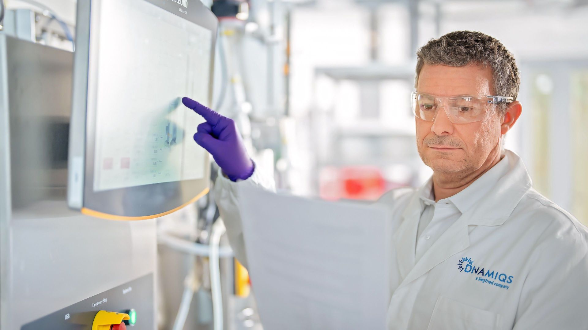 Man in lab coat and safety glasses reviews notes